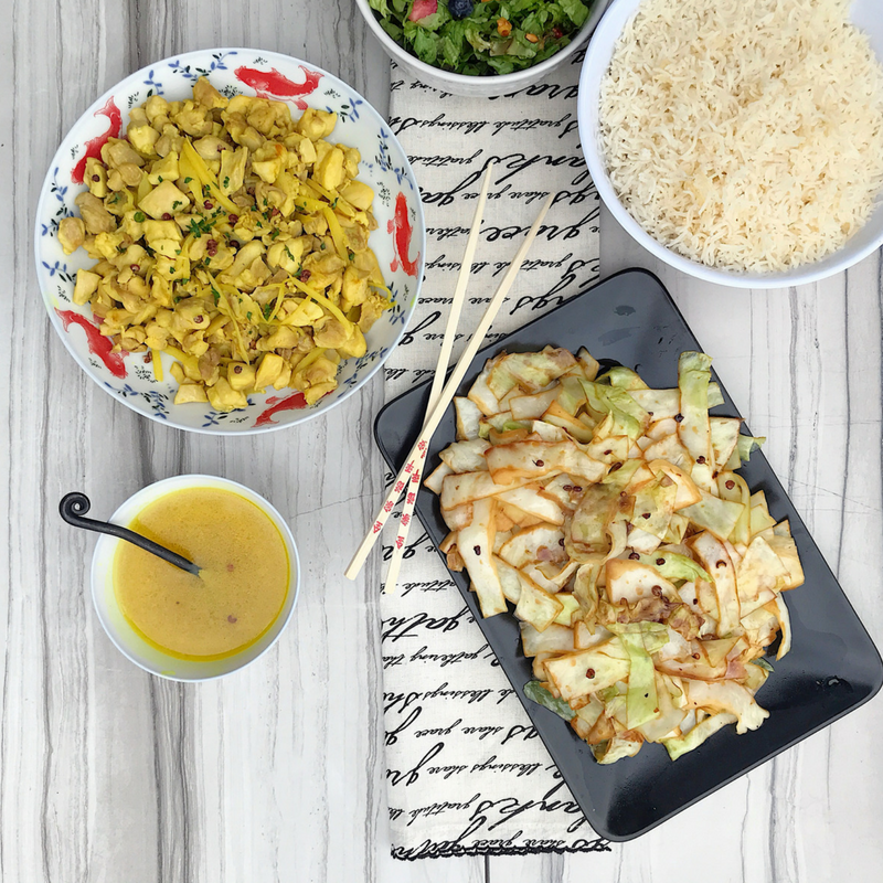 An aerial view of the ginger chicken recipe with spicy steamed cabbage, with rice and a salad. Chopsticks are displayed next to the thin-cut cabbage.